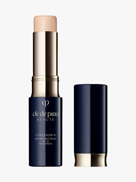 Clé de Peau Beauté Concealer navy and gold twist up concealer stick with cap to the side on light gray background